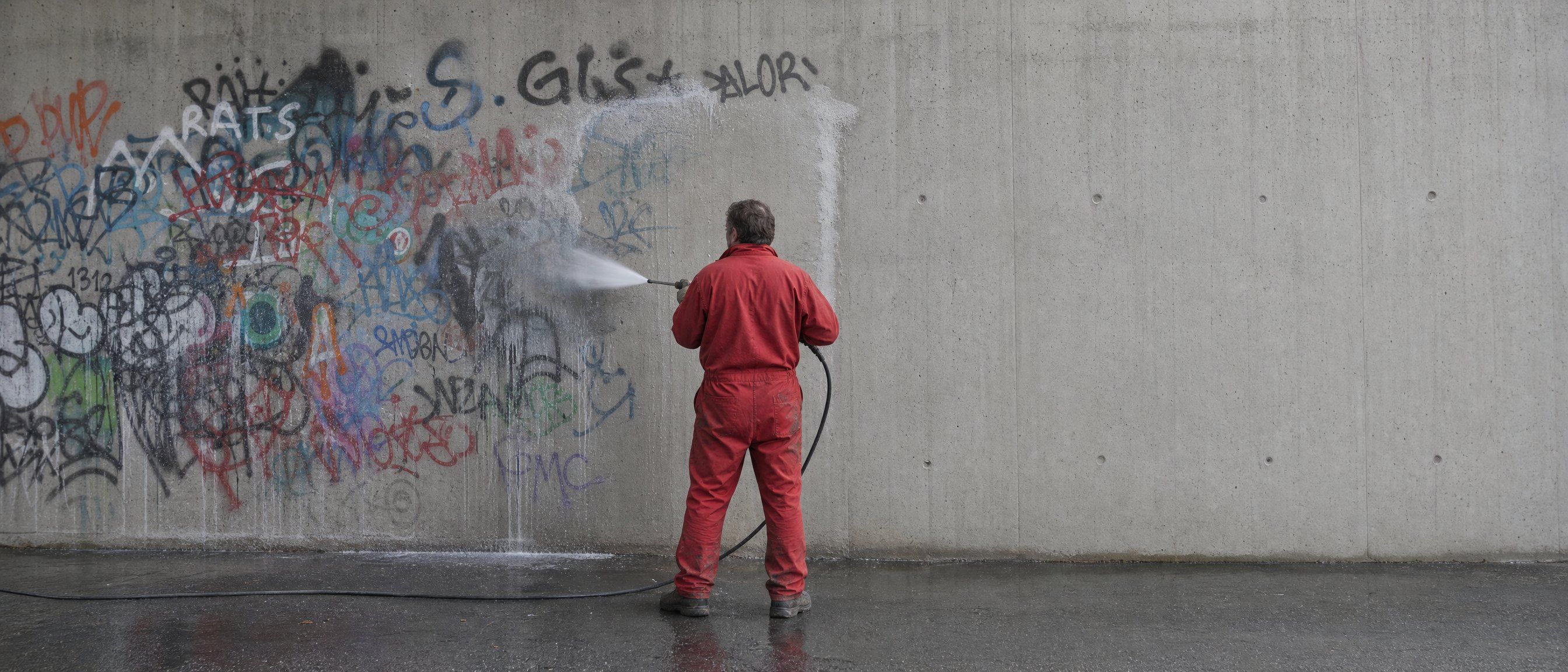 Fachkraft wäscht Graffiti mit dem Hochdruckreiniger von einer Betonwand